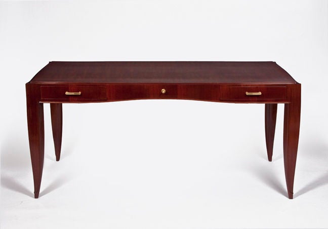 An elegant and outstanding desk by Dominique in mahogany, with elegantly tapered legs, three drawers, brass inlays and bronze details.