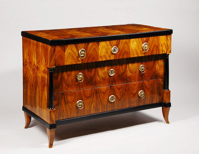 A Biedermeier three drawer commode.<br />
Bookmatched walnut veneer with engaged Doric columns, ebonized detail, and tapered sabre leg.