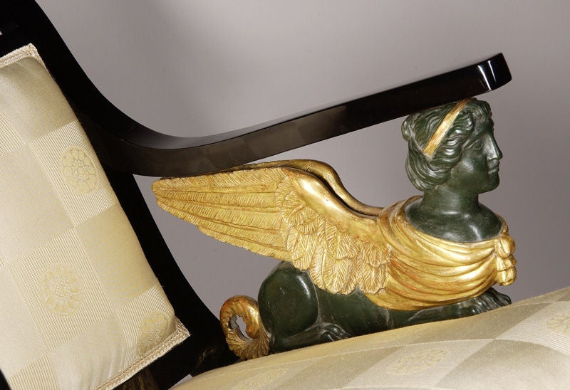 A regal Austrian Empire armchair in ebonized pear wood, carved gilt and with patinated winged sphinx arm mounts.