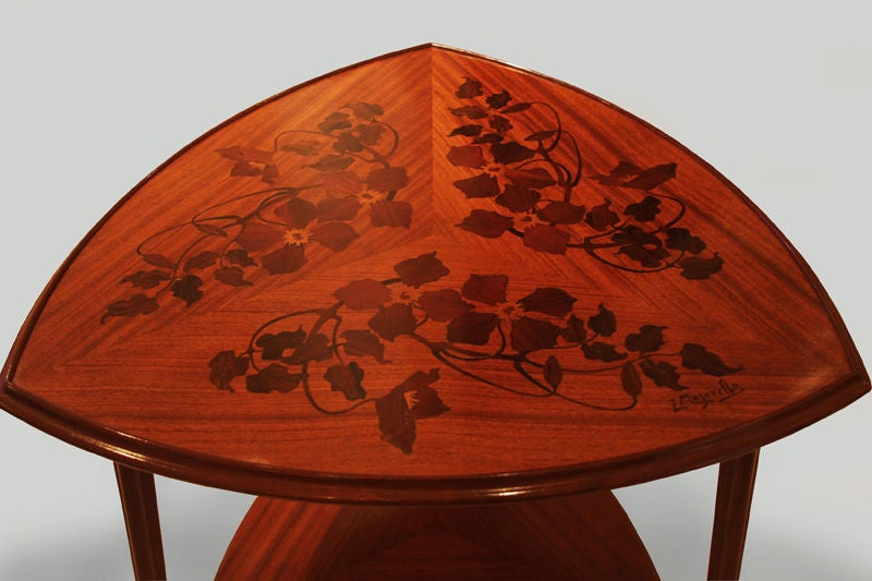 A French Art Nouveau tri-corner, two-tier table

by Louis Majorelle.

In mahogany with walnut veneer, the top inlaid in three sections with flowers and vines and signed "L Majorelle", the feet accented by orchidees gilt bronze sabots.