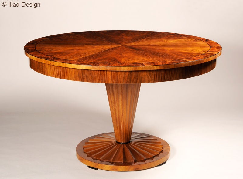 Extendable design in bookmatched walnut veneer with burled banded top. Fluted pedestal base in carved solid walnut with ebonized fruitwood detailing. Includes two leaves with four drop down legs.

Lead time required.