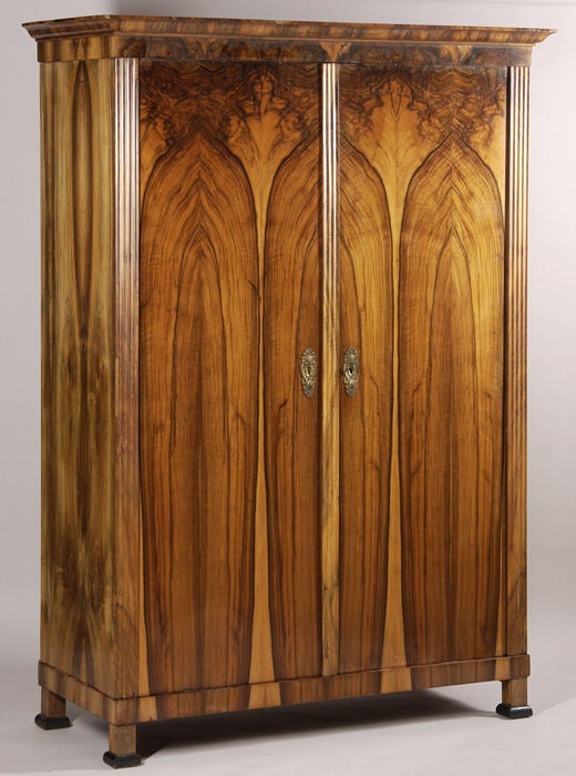 AM 20718<br />
A Biedermeier armoire<br />
Exquisite book-matched walnut veneer with fluted engaged columns and ebonized details<br />
South German, c.1825-30<br />
76.8