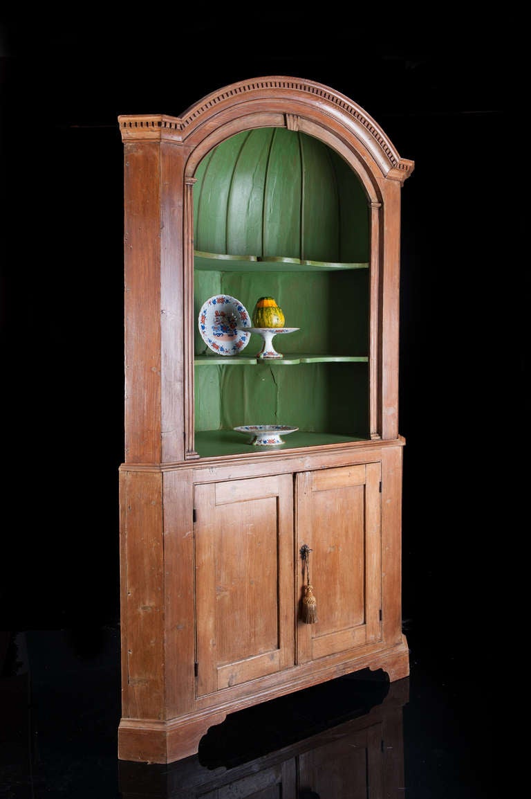 A mid-18th century Georgian period pine open corner cupboard. The upper section of with an open barrel back design with shaped shelves and architectural elements. The lower section with pair of paneled cupboard doors with a single shelf. The cabinet