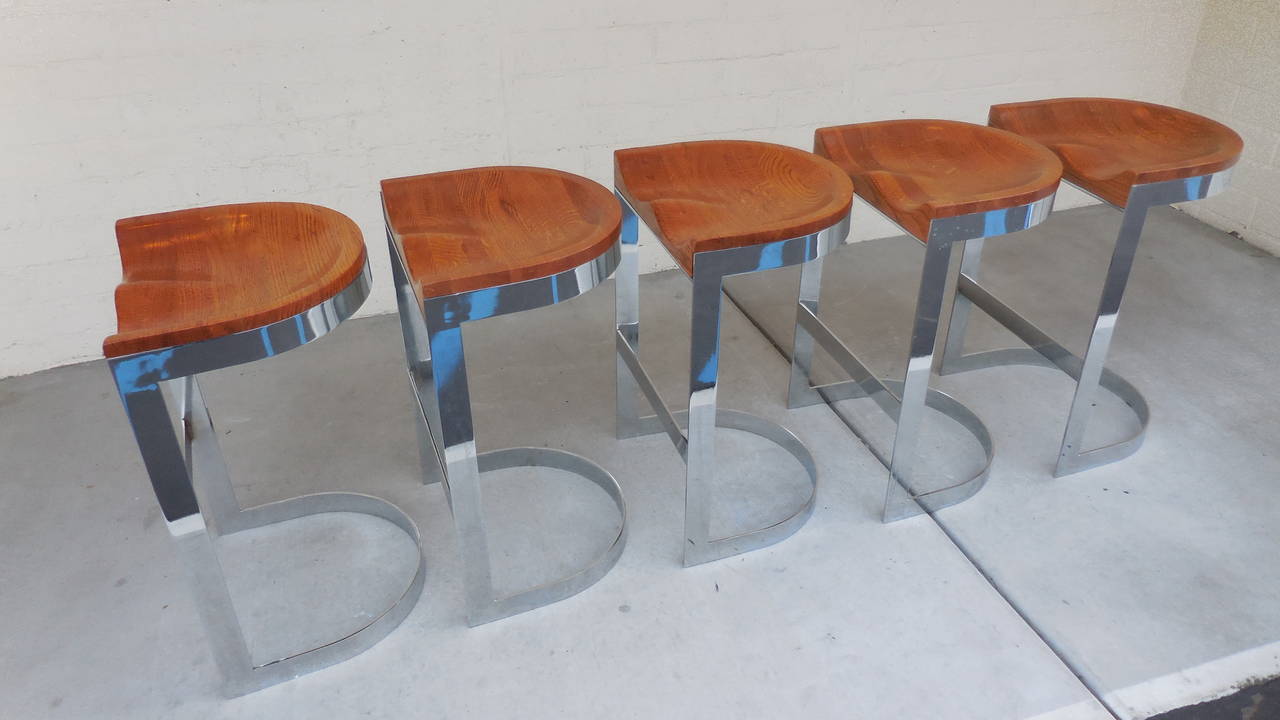 A desirable set of three counter-height bar stools designed by California craftsman Warren Bacon in the 1970s. Each stool has laminated and sculpted solid oak saddle seats that are supported by bases made of polished flat bar steel. The other