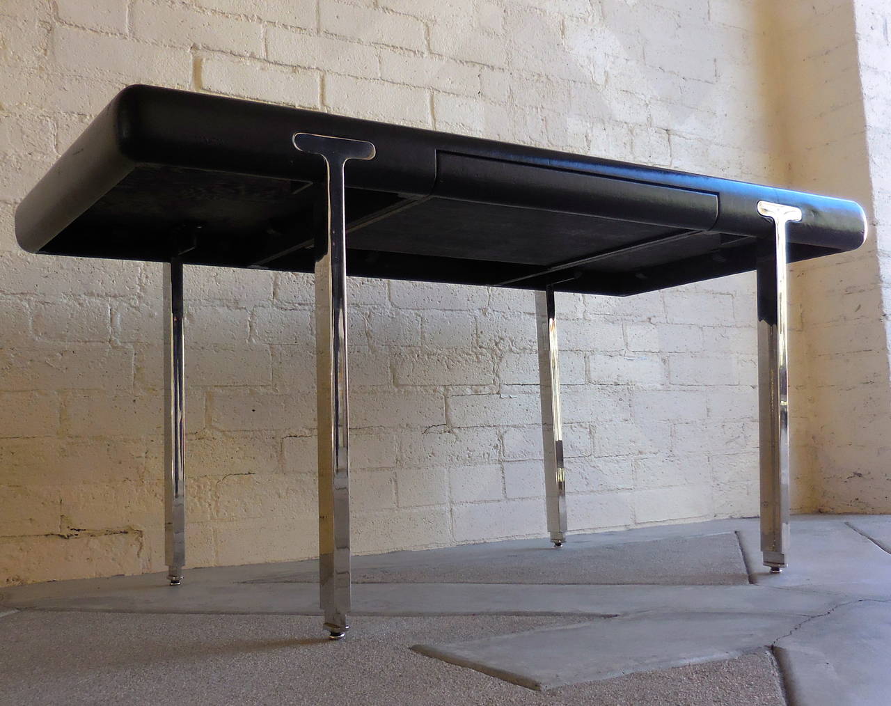 A glamorously stylish high quality black leather-clad 1970s writing table with a single drawer. A very interesting design element of this desk is the way the chrome-plated steel legs are 