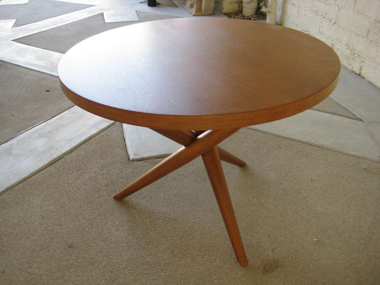 A dynamic round side table (No. 1641) in a honey toned walnut with three intersecting legs designed by T.H. Robsjohn-Gibbings for Widdicomb, 1950's.