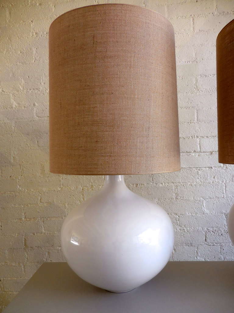 A pair of monumental pottery table lamps with a high fired white glaze from the 1980's.  The scale on these lamps is impressive and they have new linen drum shades and wiring.  The dimensions of the lamp bases alone are 20.25