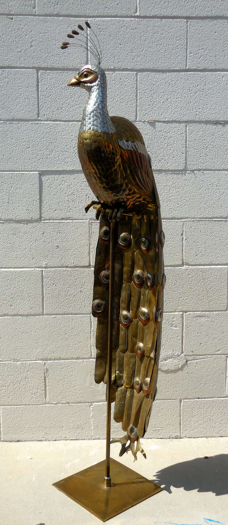 An amazing mixed metal peacock statue that sits on a brass stand by Mexican artist Sergio Bustamante, circa 1970s.  The peacock is a symbol of integrity and immortality and although other fowl pieces by Bustamante are available, peacocks are rare