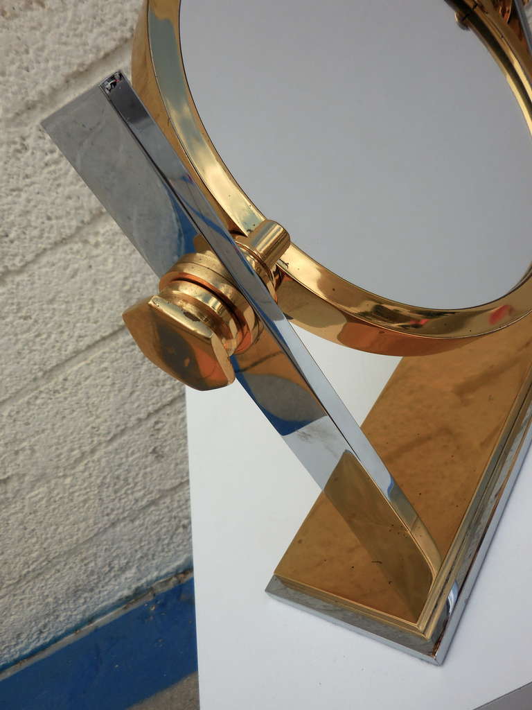 A very desirable chrome and gold plated vanity mirror by Karl Springer  C. 1980.  This heavy-duty make up mirror is two sided, with one of the mirrored surfaces being a magnifier.  The side bolts loosen, allowing the mirror to pivot.
