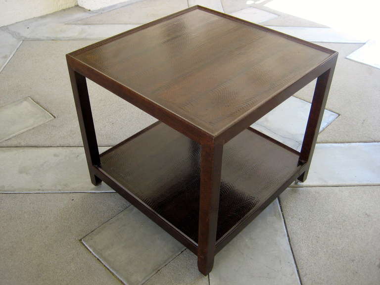 A snakeskin covered two-tier square side table with brass casters by Karl Springer. This side table is a significantly larger scaled version of Springer's iconic telephone table.