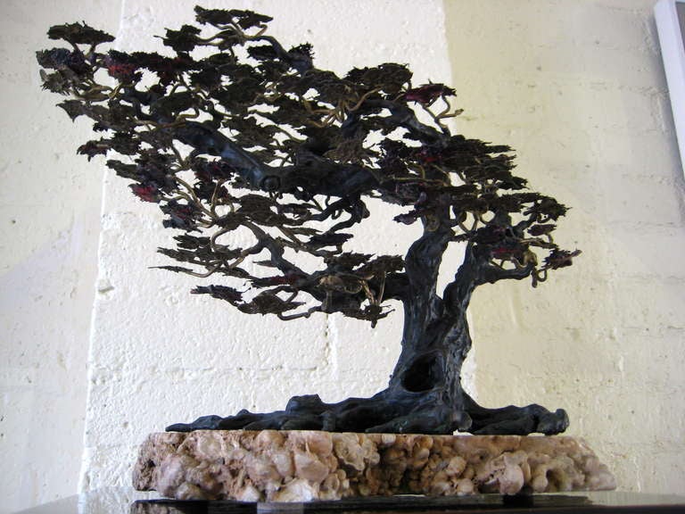 A bronze bonzai tree, naturalistically sculpted and mounted on a petrified wood slab base.  The leaves of the tree are made of brass and copper, which has been colored to mimic a seasonal (Autumnal) change.  The trunk, limbs and roots of the tree