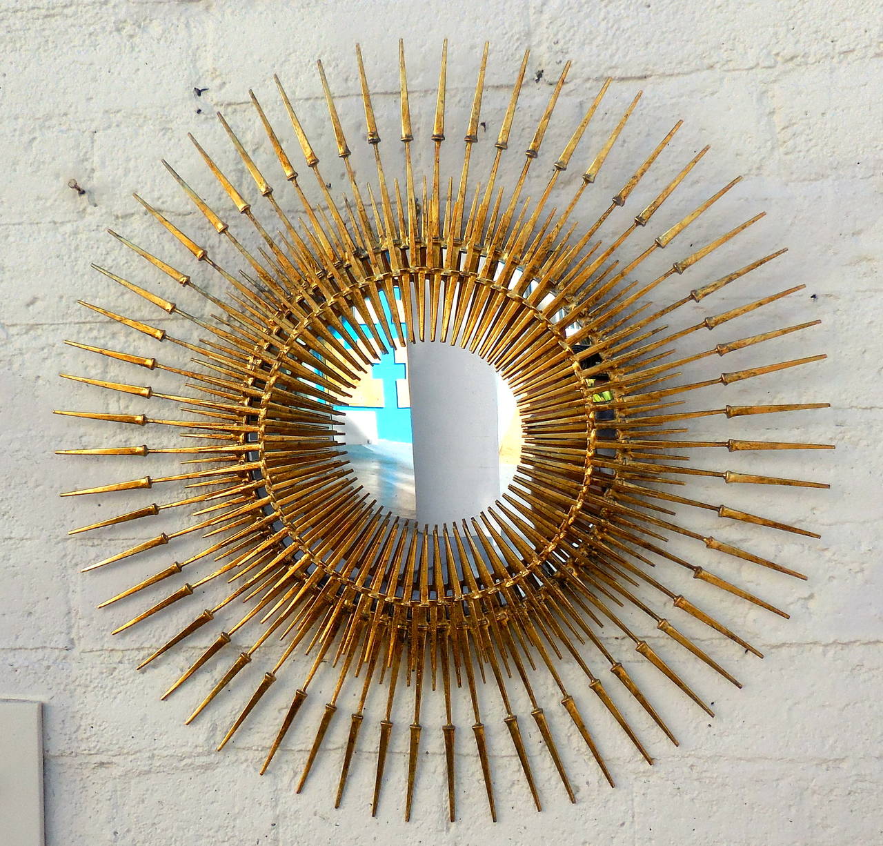 An intensely dynamic radiant starburst mirror by American sculptor Del Williams. Signed and dated 2015. Using traditional welding techniques this custom fabricated sculpture is composed of hundreds of hand gold leafed spikes that are welded together