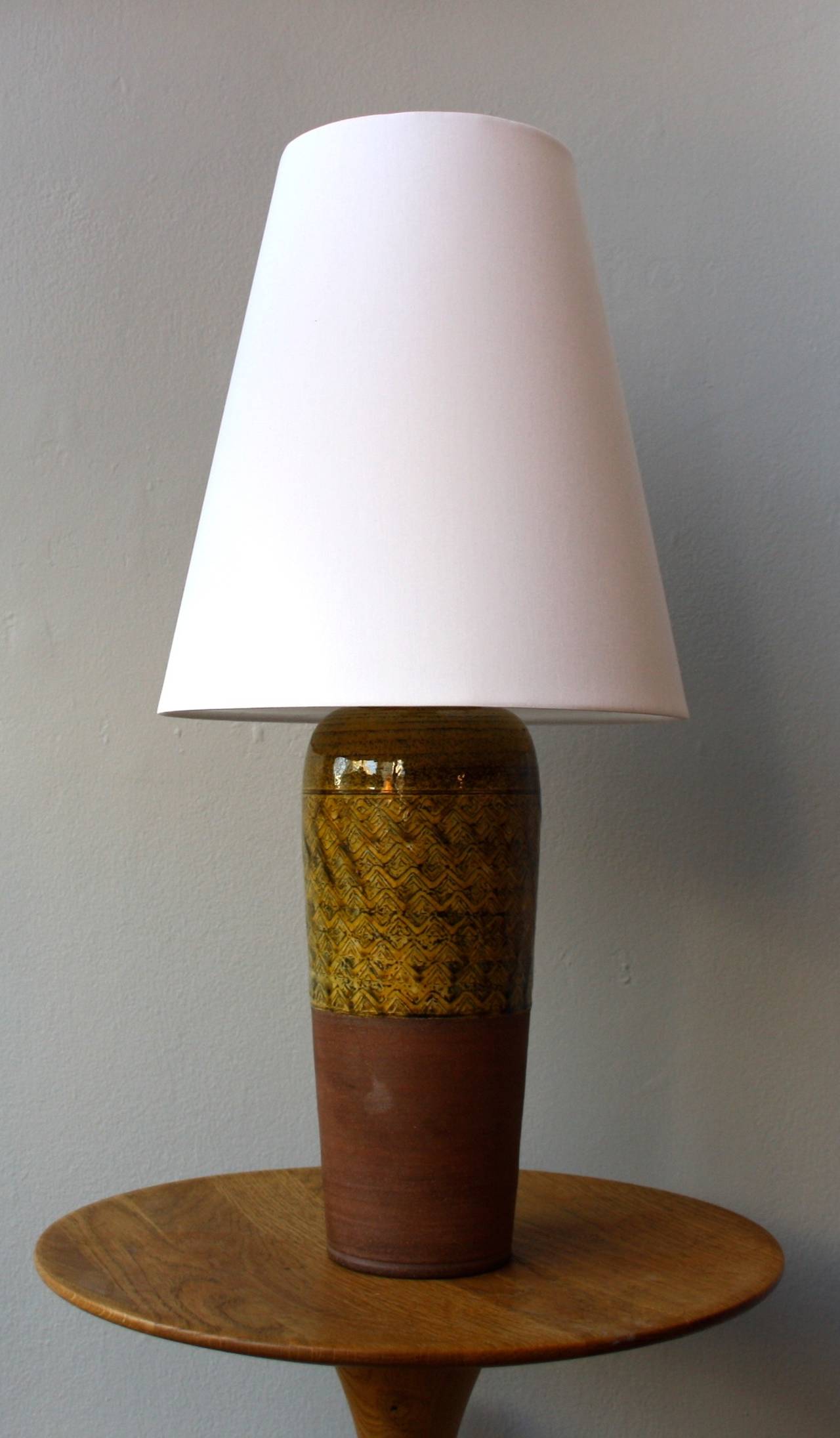 Herman Kahler's workshop. Great hand-thrown table lamp with the upper part wonderfully covered by a yellowish textured glaze. The lower part unglazed bears the warm brown colour of earthenware. Topped by a new white cotton shade.