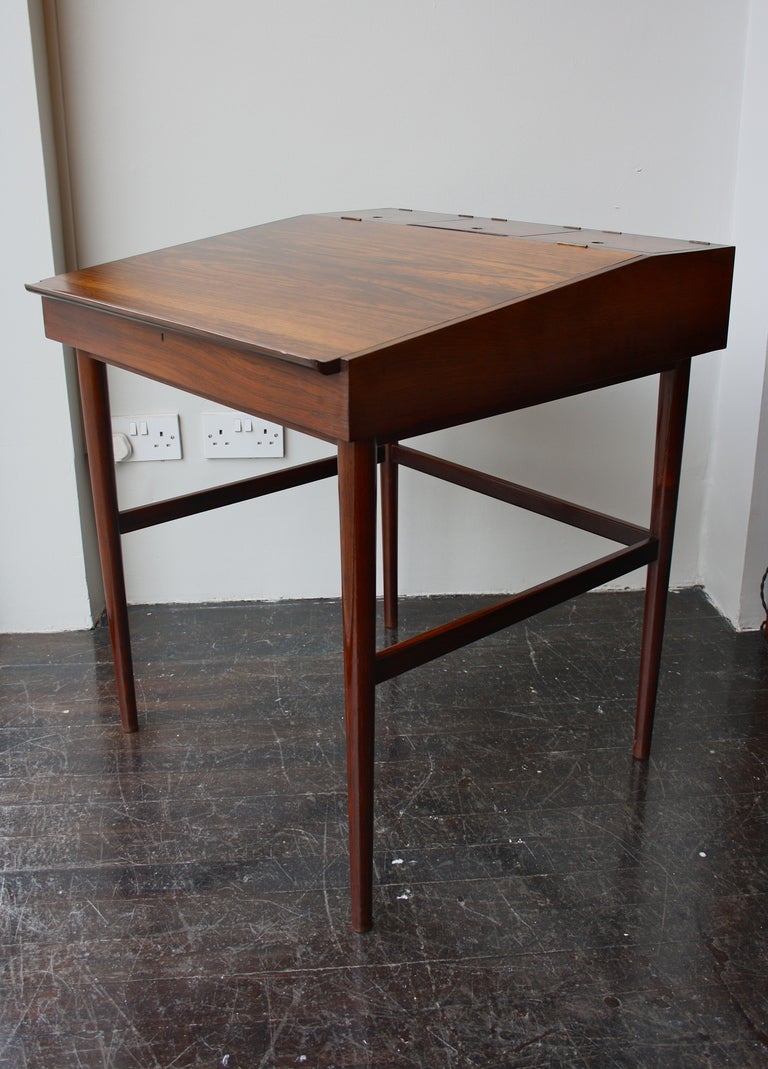 Great small desk by the magical combination of Finn Juhl and mastercabinetmaker Niels Vodder. Brazilian Rosewood and brass details for the handles and fittings. Opens up to reveal a large compartment under the slope. Three more compartments on the