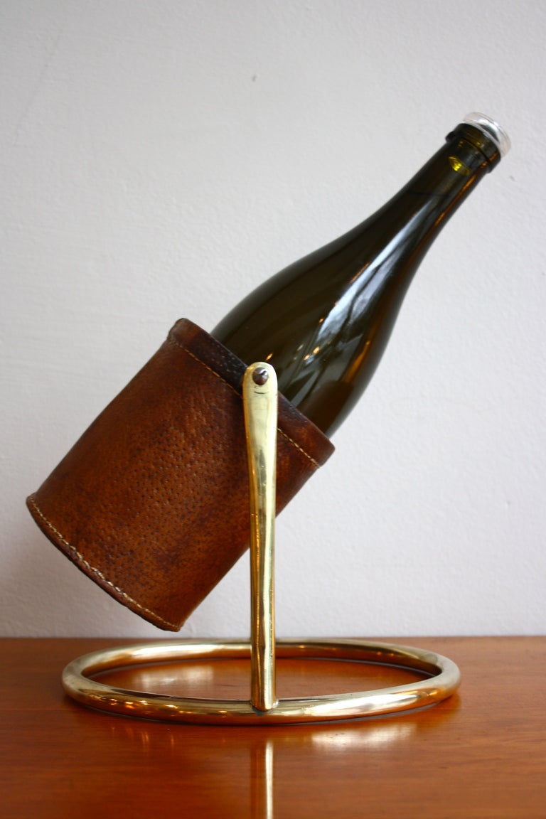 An elegant brass and leather bottle holder by Carl Auböck the Austrian brass master. This handsome wine bottle holder has its  original matured leather cup and a grand brass base marked with Auböck's unique impression.
