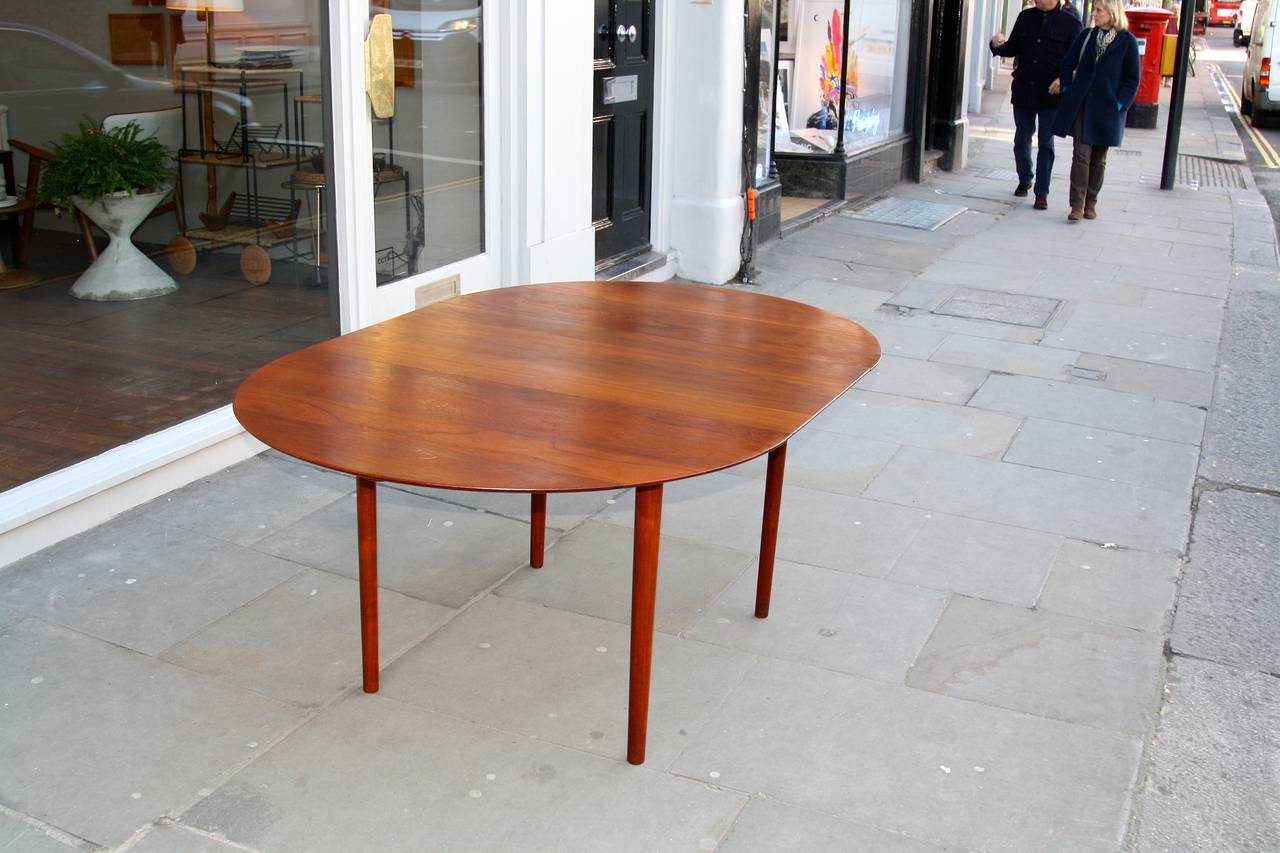 Great oval solid teak dining table with one leaf. The solid top looks floating and thin with the chamfered edges. Very well made and in great condition.