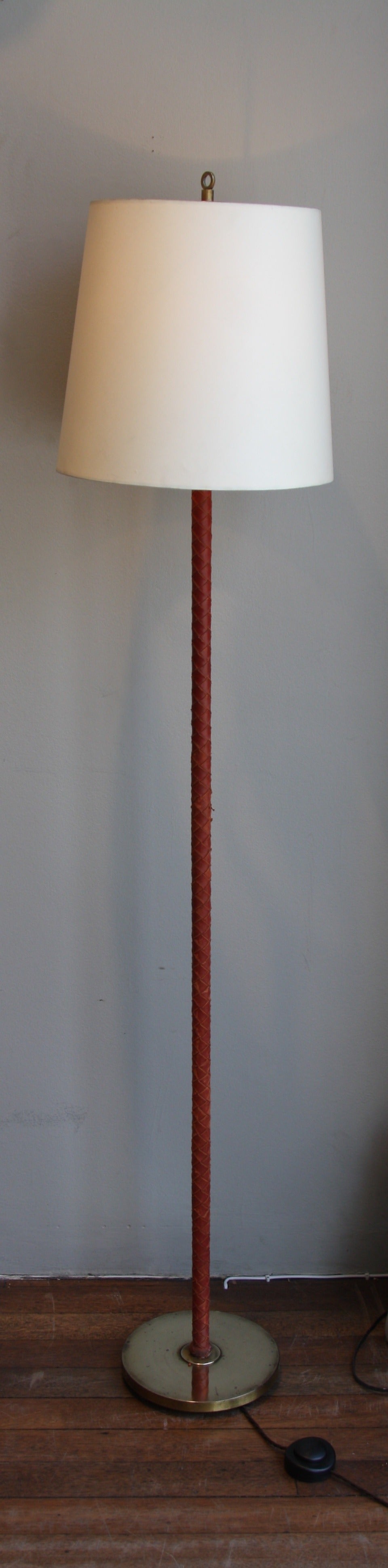 Woven red leather stem floor light with a brass foot and finial.