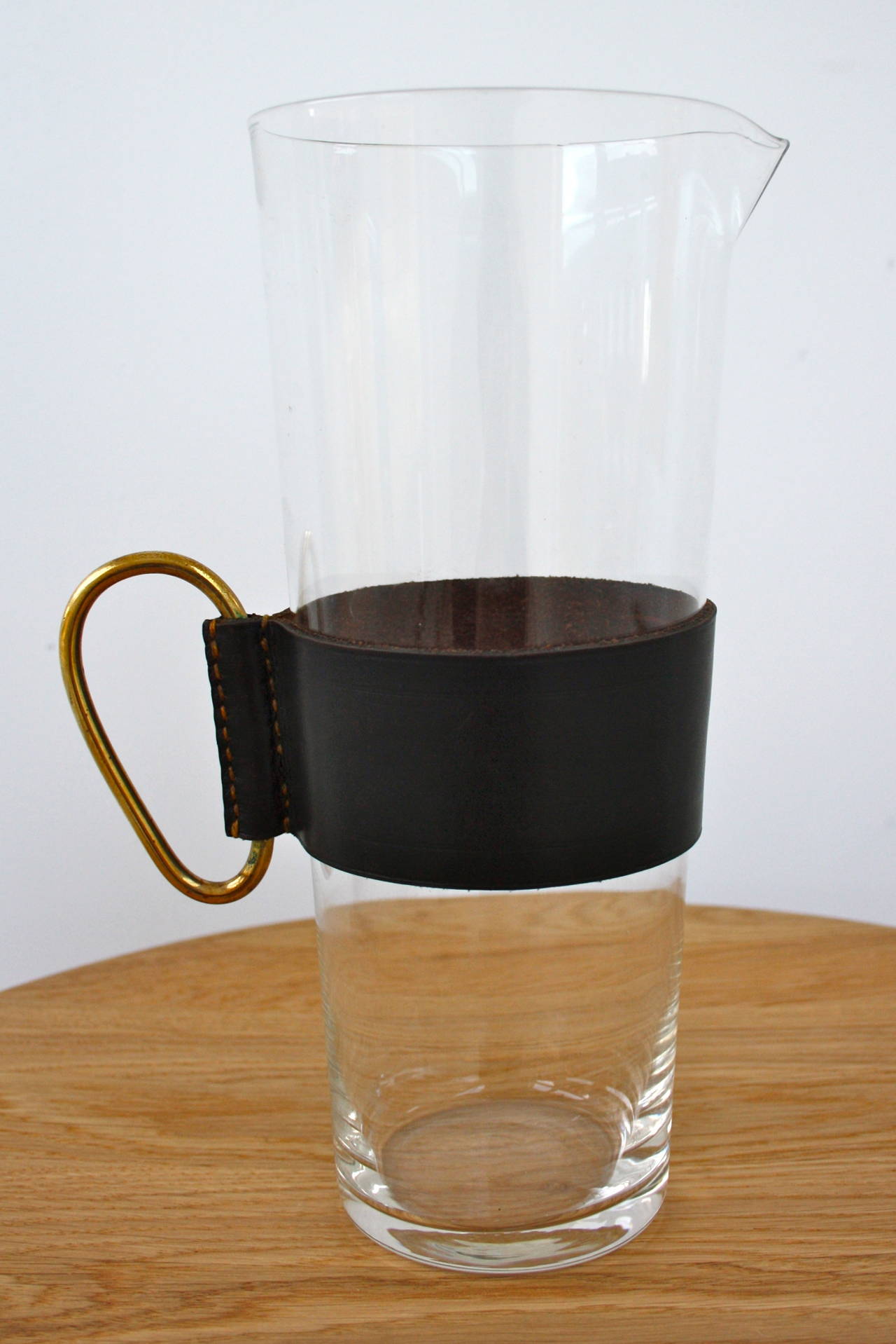 A large glass jug from the Carl Aubock Workshop. The jug is strong and tall, great for entertaining. Easy cleaning as the beautiful black sleeve slides straight off. Attached to the sleeve is solid brass ring handle, cast in the workshop, its