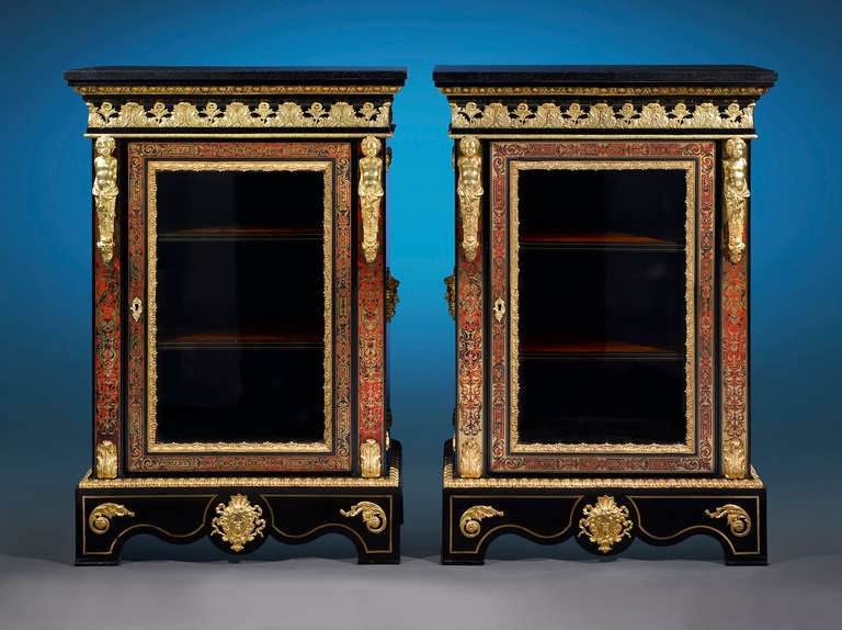 This exquisite pair of French cabinets bears the unmistakable decoration known as Boulle marquetry. Accented with finely cast doré bronze mounts in the form of putti herms and grotesque masks, these exceptional glass-front cabinets are adorned with