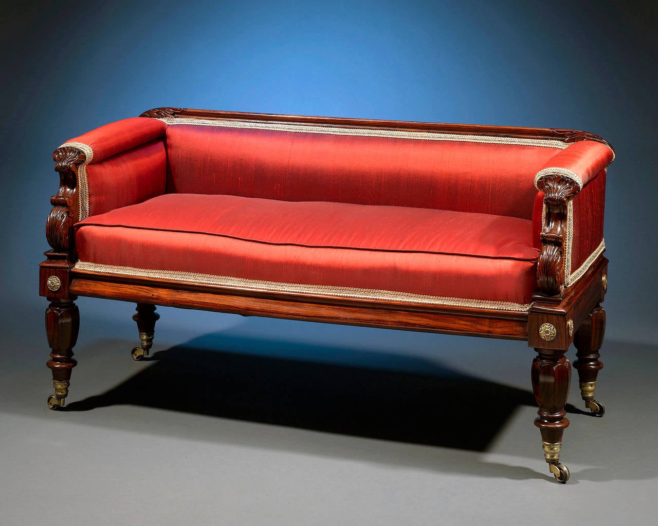 This important Regency-period settee is crafted of handsome rosewood and displays wonderfully detailed carving. Exhibiting an exceptionally rare diminutive form, this enchanting seat boasts classically inspired elements, including the acanthus leaf