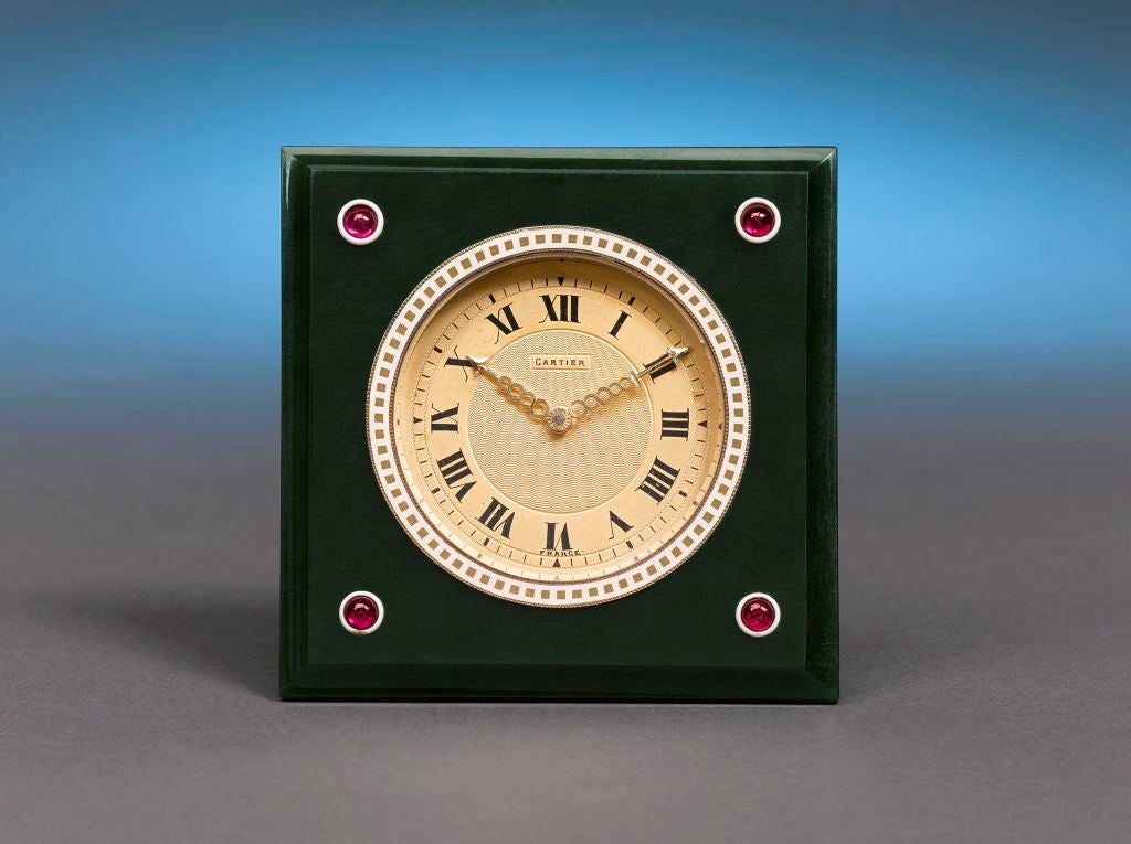 This exquisite Art Deco travel clock by Cartier features a lustrous jadeite frame studded with four ruby cabochons. The expertly crafted 8-day movement tells time on an engine-turned silver dial set within delicately enameled bezel. With Roman