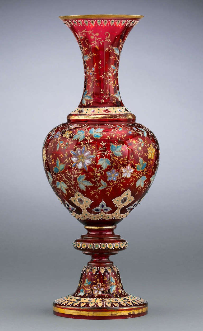 Almost certainly made as an exhibition piece, this monumental Moser ruby glass vase boasts a gilt-accented design of textured oak leaves and flowers, all enclosed by textured bands of jeweled gilding. Formed in a classical urn shape in Moserâ??s