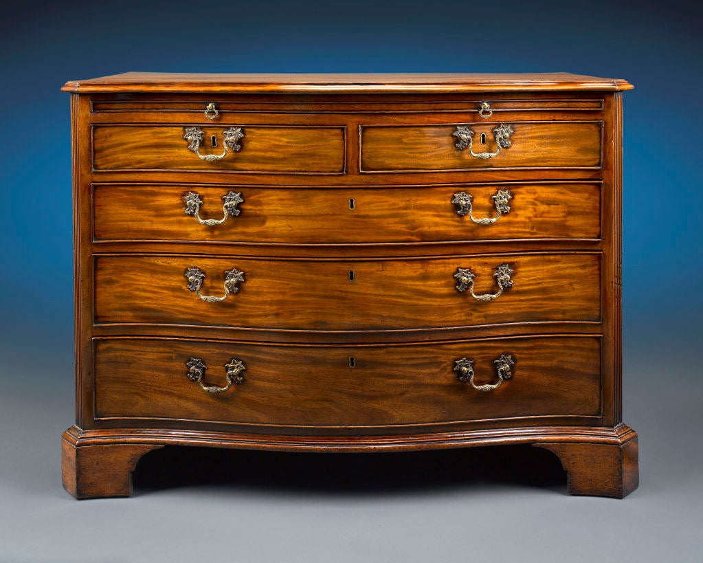 This rare 18th-century chest of drawers is both practical and luxurious. Crafted of mahogany during the early Georgian period, this chest exhibits the elegant neoclassical style, with a dramatic serpentine façade framed by fluted, canted corners.