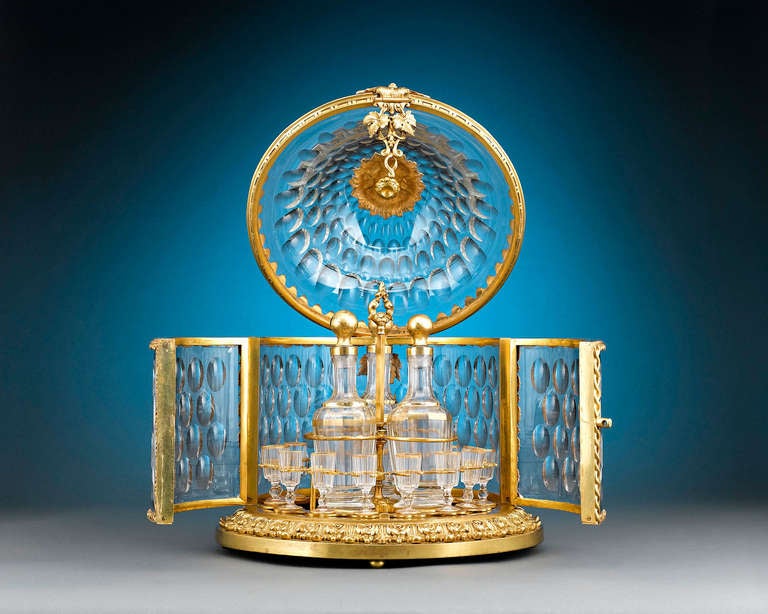 A stunning Napoléon III-period cavé liqueur crafted of glorious Baccarat cut glass and doré bronze. An opulent classical motif informs every aspect of this lush design. The footed case is crafted in the ancient Greco-Roman style, with a ring of lush
