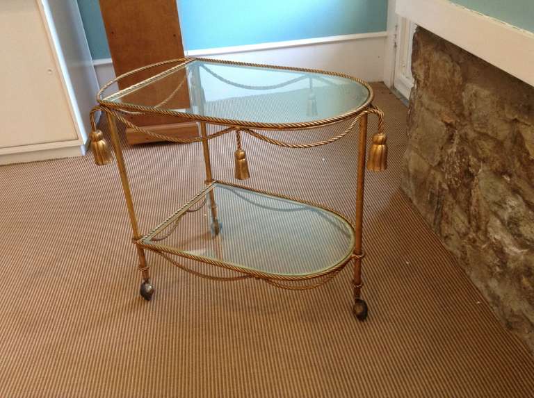 Unusual gilt metal, two tier drinks or tea trolley with glass shelves. The trolley has a very decorative tassel and rope design on wheels for ease of movement.