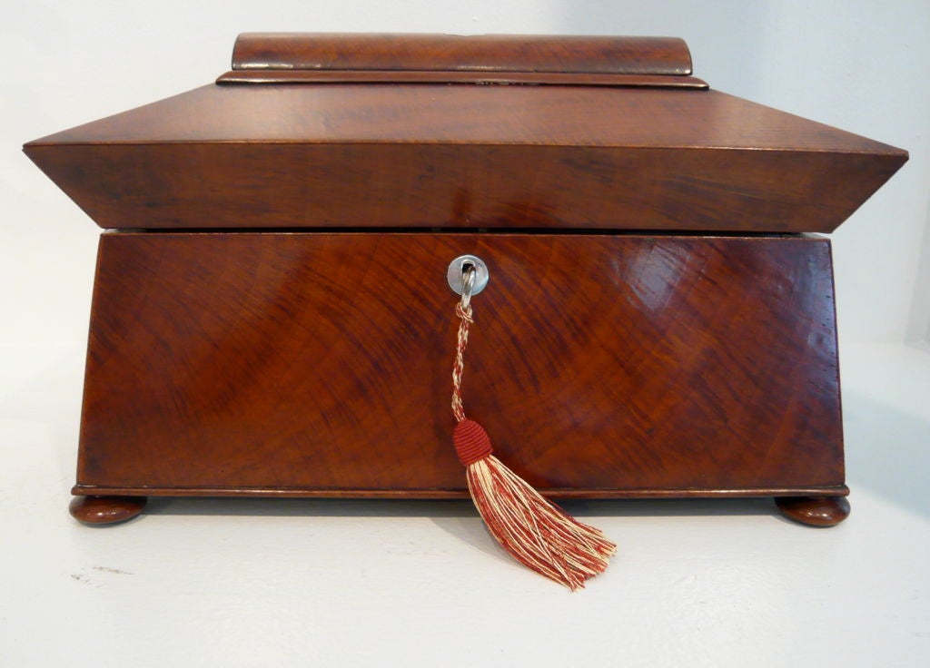An early English Victorian mahogany tea canister of sarcophagus form. The lid is inset with a silver initialed cartouche and opens to reveal a fitted interior of two hinged lid boxes and an etched glass mixing bowl.