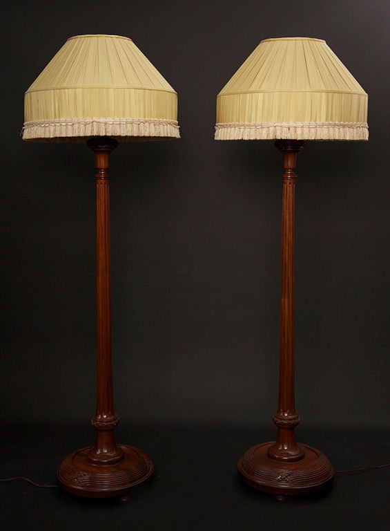 Pair of intricately carved Mahogany base floor lamps, perfect for a boudoir, master suite or salon. Circa 1930's these Art Deco lamps boast carvings and detail throughout, from base to fixture. Shades are original, with slight wear, pink satin