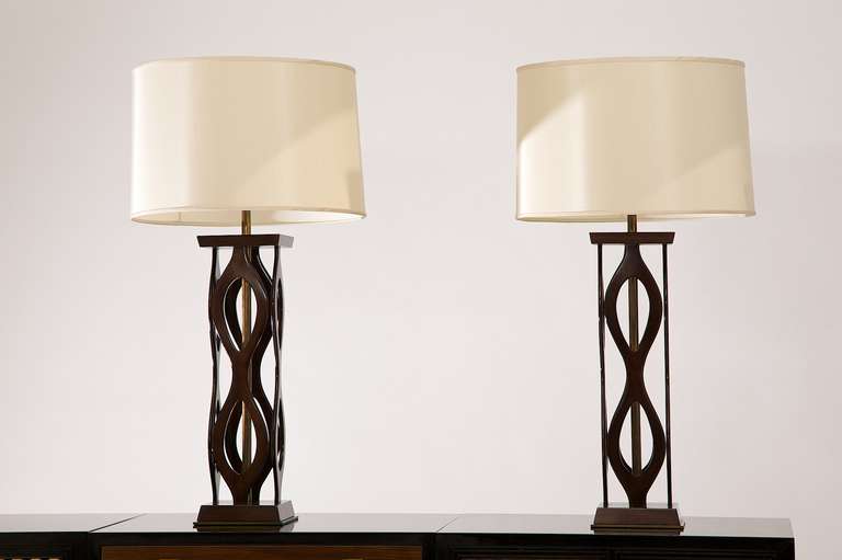 A refined pair of modernist lamps in lacquered mahogany with brass accents. The lamps are finished off with bone colored silk shades in perfect condition with the original finials. Makes a fine addition in a bedroom or living room setting. The lamps