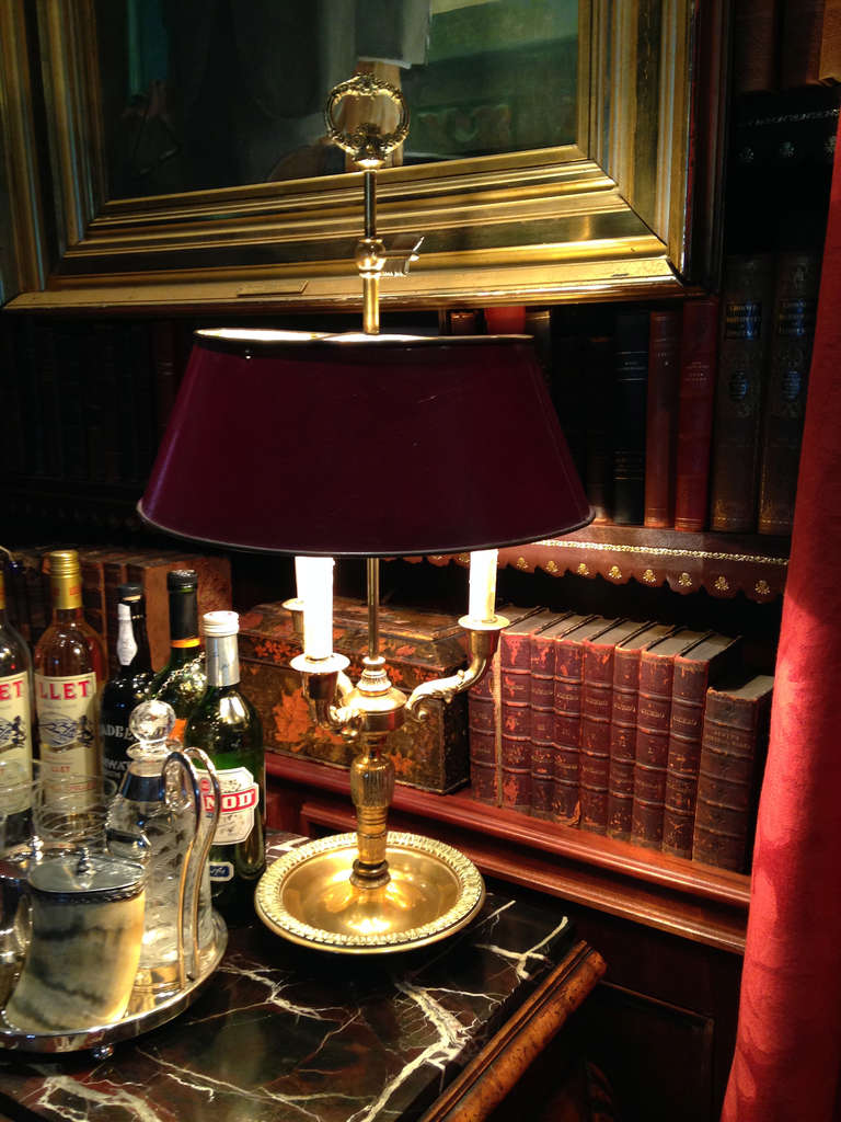 French Bouillotte lamp with a decorated brass base, three arms with painted faux wax sleeves, the tole shade painted a deep red with a brass lining. The center brass rod terminates in a finial with an arrow. In-cord switch. Very good antique
