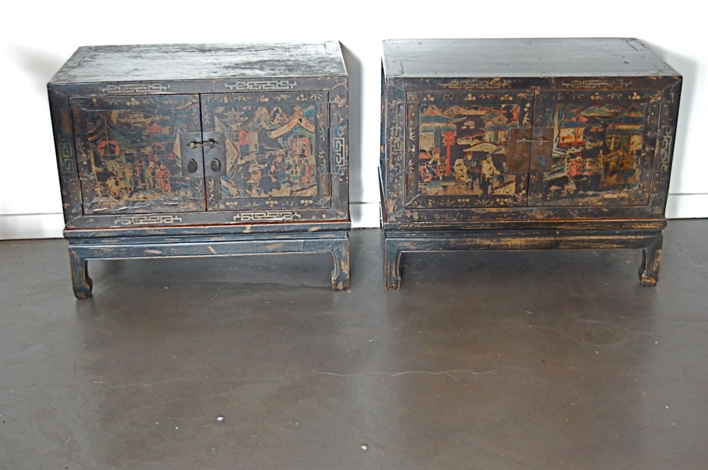 A pair of Asian painted trunks on stands, consisting of two cabinet doors with iron escutcheons, opening to reveal a Chinese red interior, the simple base raising the trunk.