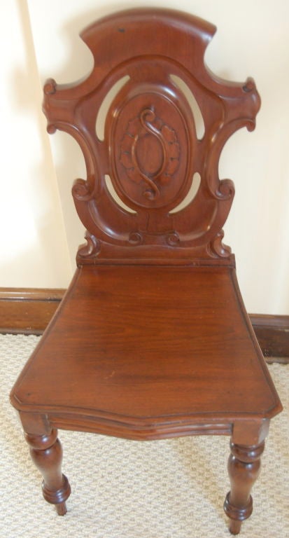 Pair of late 19th century English mahogany shield back carved and decorated hall chairs, the backs with a center medallion and the legs simply turned.