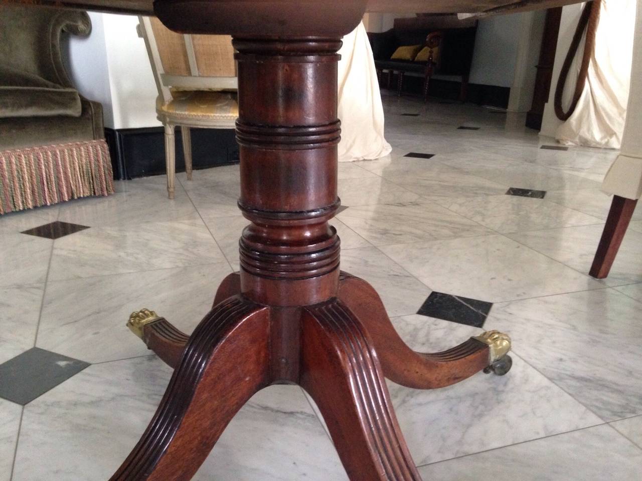 Georgian tilt-top mahogany breakfast or supper table, on tripod pedestal base, with brass lion's paw casters, inlay banding on top perimeter. Seats six comfortably. Will fold flat against wall (see photograph).