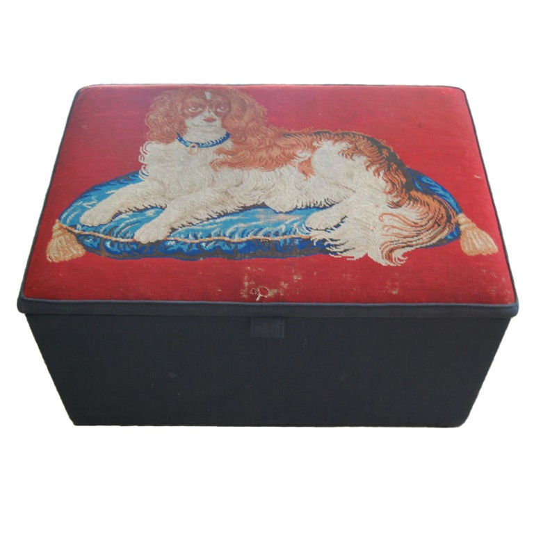 Hinged storage box/ottoman/coffee table upholstered in black linen with a 19th century needlepoint top depicting a King Charles spaniel on a red ground.
