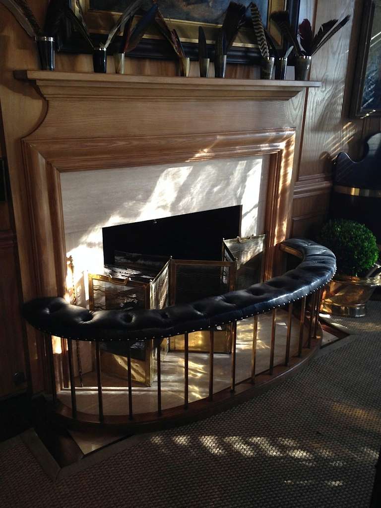 An unusual arc-shaped oak, brass and tufted black leather fireplace club fender with an elegant bend and a generous size providing extra seating by the fire in great style.