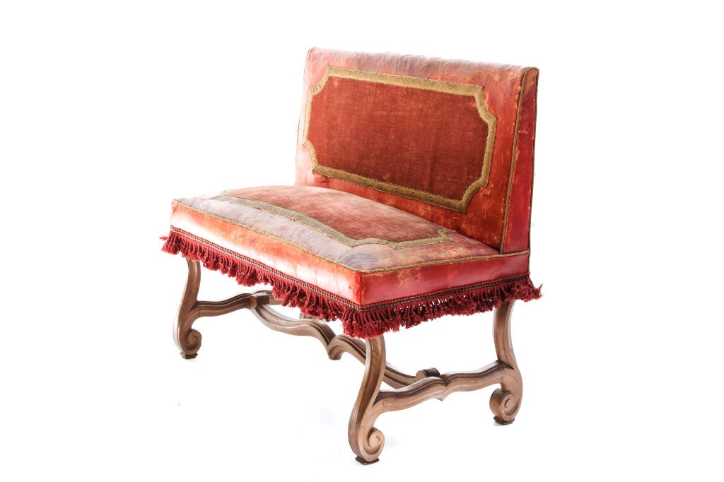 Red leather with velvet insets on seat and back bordered with gold edging, brass upholstery tacks and cotton fringe, on a curving wood base with stretcher.