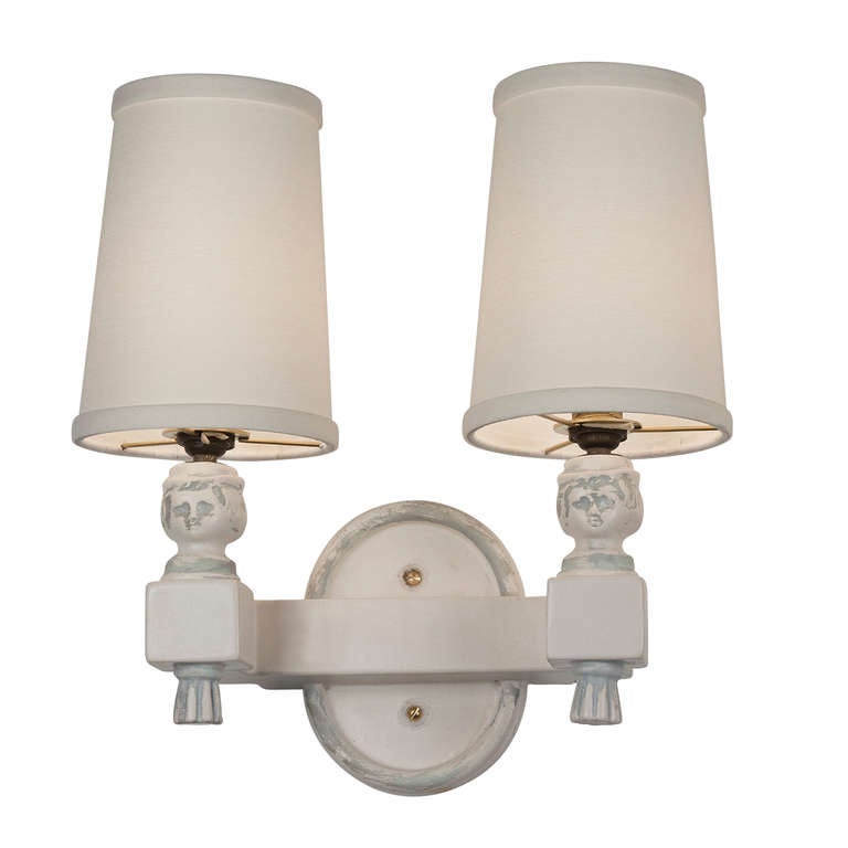 Antiqued ceramic two arm sconces, the two curved block arms emanating from a center oval backplate, with female head form on each arm, just below custom shades. Shades measure top diameter 3 in, bottom diameter 4 in, height 6 1/2 in. In the style of
