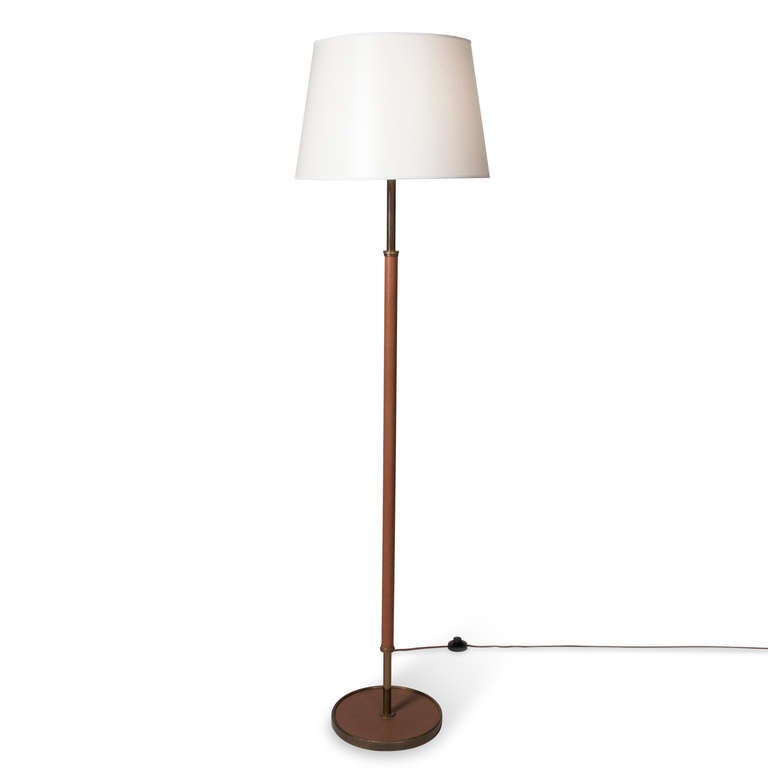 Textured leather floor lamp, hand-stitched, the base a leather covered circular disc with brass border, having brass rod neck, attributed to Jacques Adnet, French 1950s. In custom silk shade. Overall height 68 in, base diameter 11 1/2 in, shade