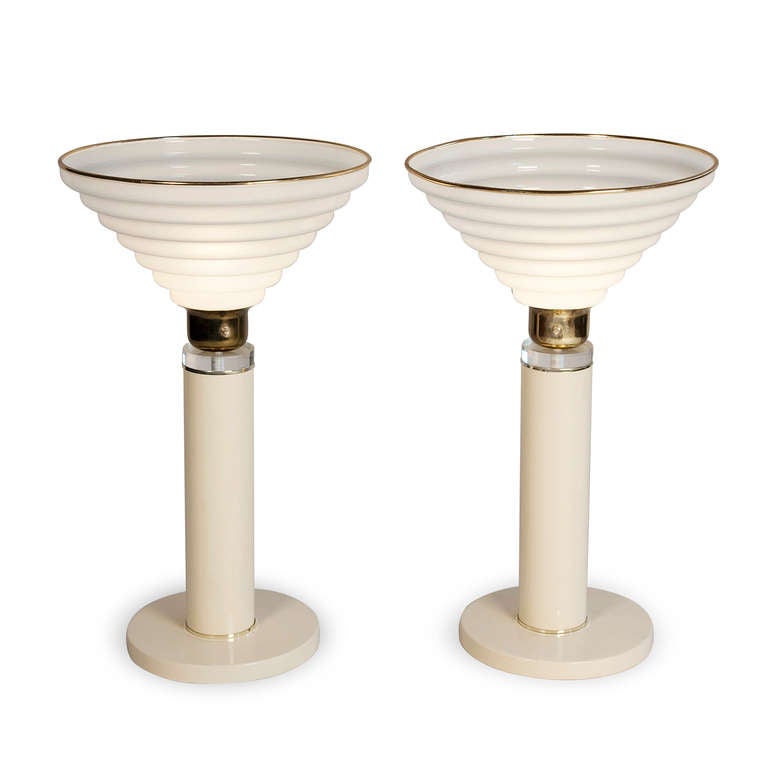 Pair of enameled metal and plexi table lamps, the off-white color metal base a circular column supporting a frosted white stepped inverted cone shape plexi shade, with brass and lucite bands between the two elements, and having brass edging at top,
