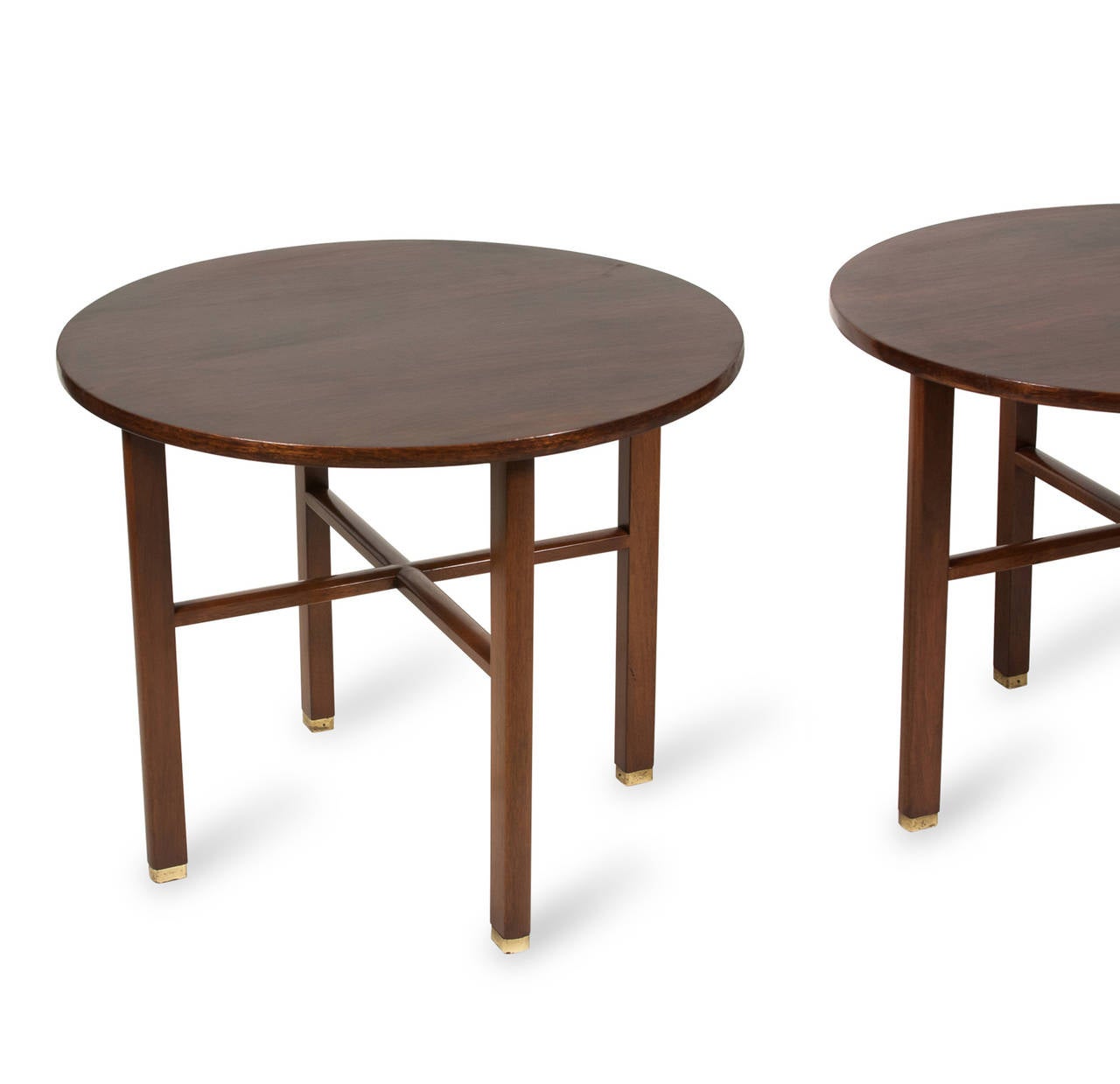 Mahogany occasional or end tables, circular top on four rectangular legs, joined by an X-stretcher, brass cap feet. By Dunbar, American 1950s. Stamped to underside. Height 22 1/2 inches, diameter 27 inches. (Item #2218)