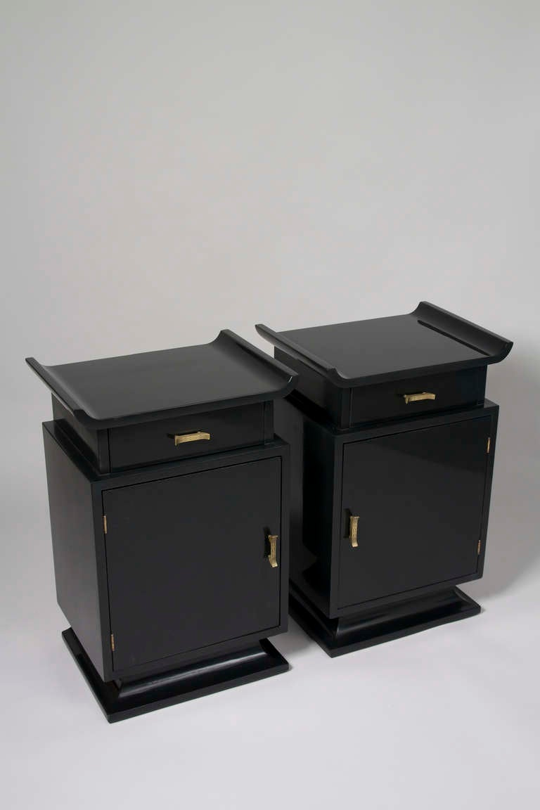 Pair of black lacquered Asian Modern nightstands or end tables, the top surface having upturned sides, with a single drawer over a door concealing a storage compartment, on tapered plinth base with textured bronze pulls, in the style of James Mont,