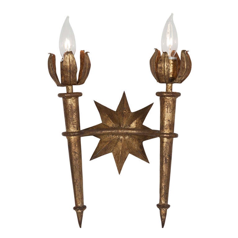 Pair of two arm torch form dore metal wall sconces, the torch tapering and finishing with petal flame bulb surround, with center star form, in the style of Gilbert Poillerat, French 1940s. Height to top of bulb 17 1/2 in, width 10 1/2 in. 
Price