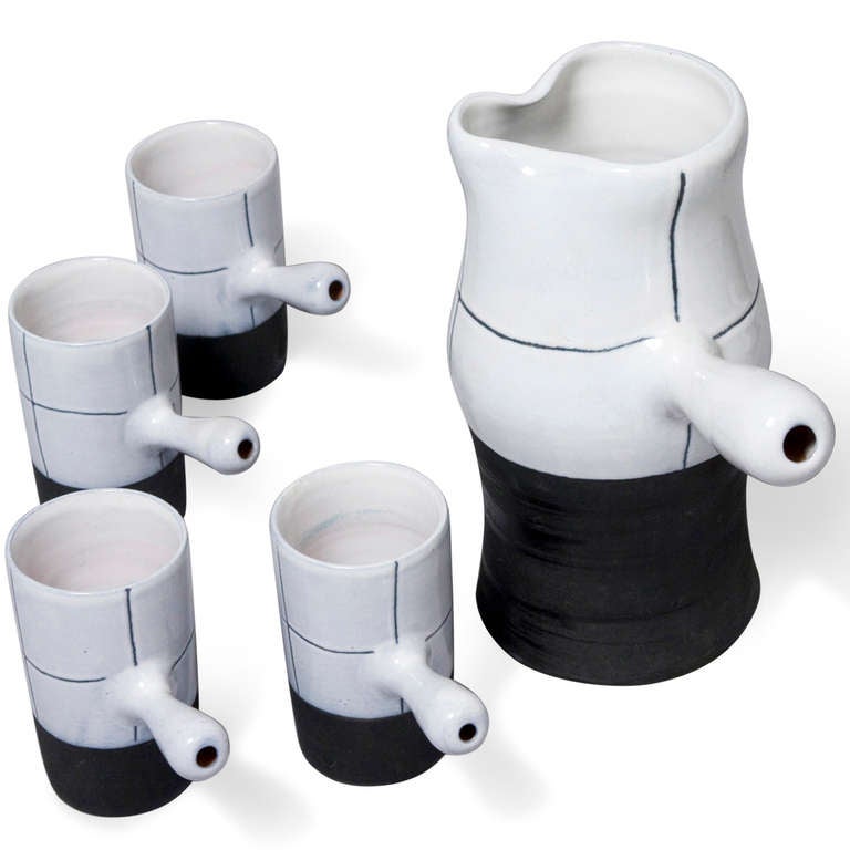 Five piece coffee or mocha service, a handled pitcher and four handled cups, each of white ceramic with black sgraffito markings and black lower half. By Jacques Innocenti, French 1950s. Signed to underside. Height of pitcher 9 in, largest diameter