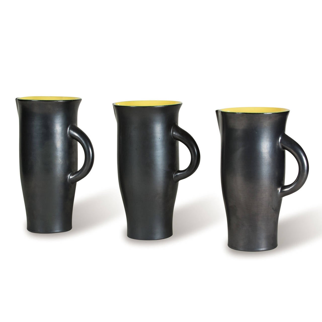 Set of three black glazed ceramic pitchers, the interiors glazed bright yellow, of slightly different for, in a lustre finish, by Elchinger, French early 1960s. Height of tallest 11 1/2 in, diameter of largest (excluding handle) 5 3/8 in. Signed to