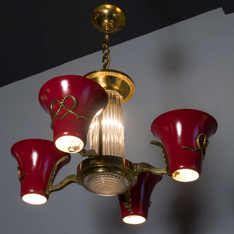 Lacquered tole and brass chandelier, four arms each ending in an inverted tapered red lacquered cone, and a center column of thin glass rods, by Petitot, French 1930s. Diameter from end of shade to end of shade 25 in, height of fixture not including