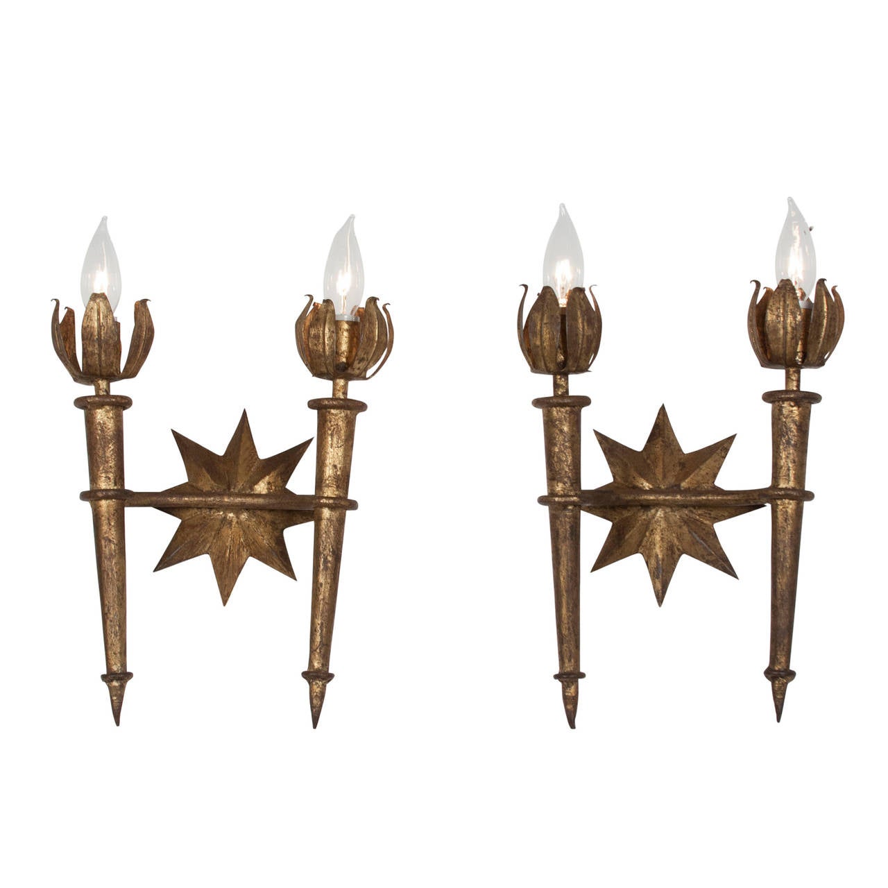 Pair of two arm torch form dore metal wall sconces, the torch tapering and finishing with petal flame bulb surround, with center star form, in the style of Gilbert Poillerat, French 1940s. Height to top of bulb 17 1/2 in, width 10 1/2 in. 
Price