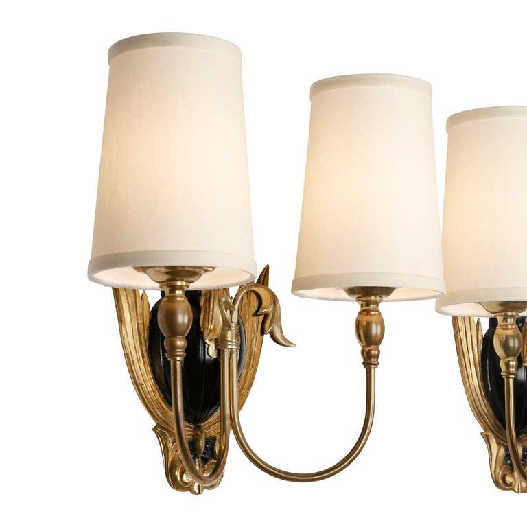 Pair of gilt and lacquered carved wood wall sconces, the black lacquered urn shaped wall mount flanked by giltwood foliates, each sconce with two looping brass arms, in custom silk shades, French, 1940s. Overall height 14 1/2 in, width 13 1/2 in,